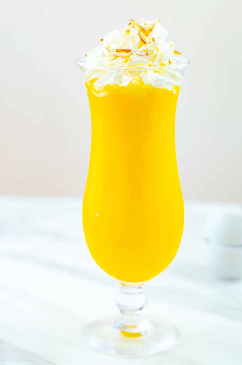 mango milkshake in a tall glass with a whipped cream on top.