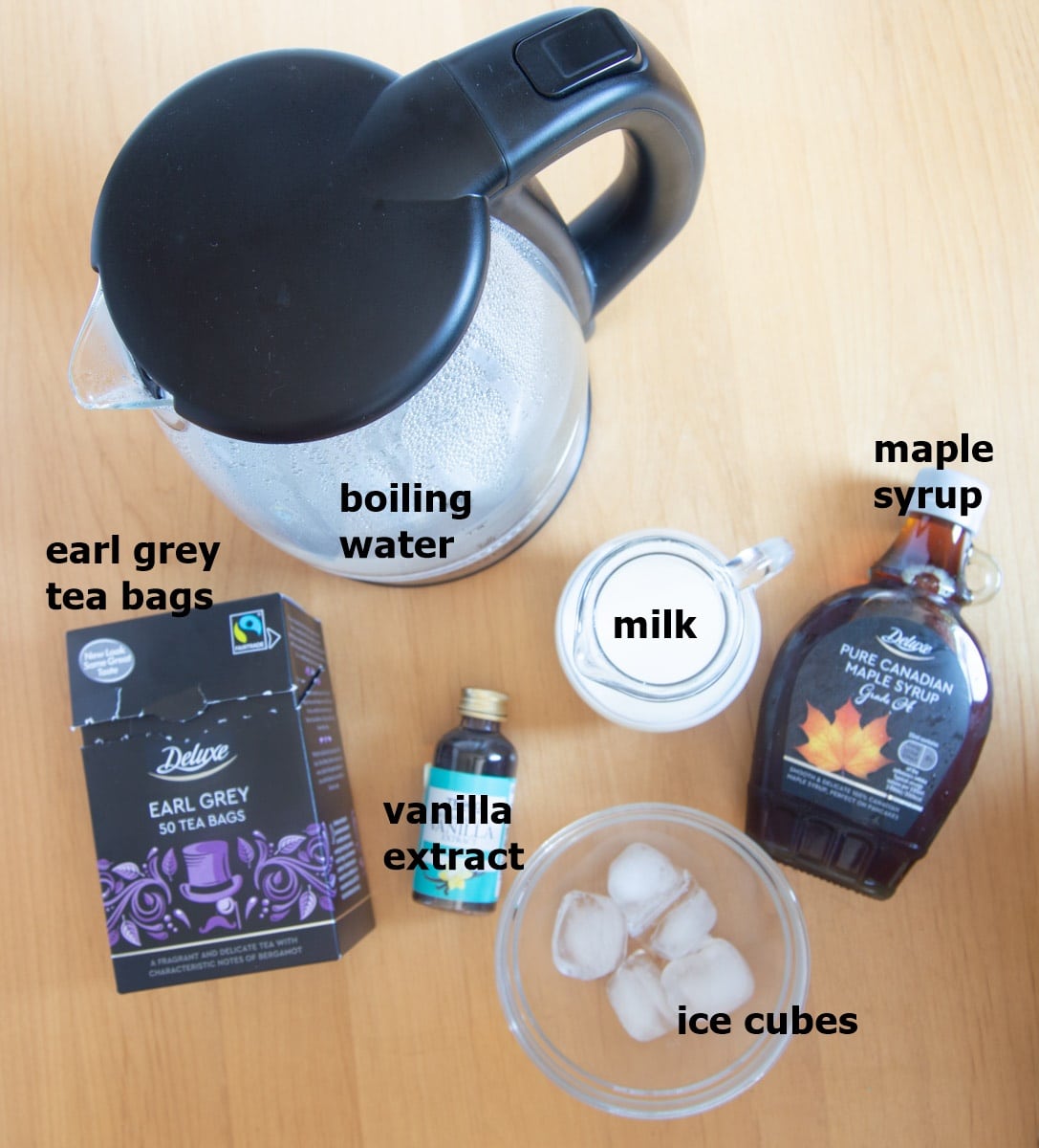 boiling water, earl grey teabags, ice cubes, milk, vanilla extract and maple syrup on wooden table.
