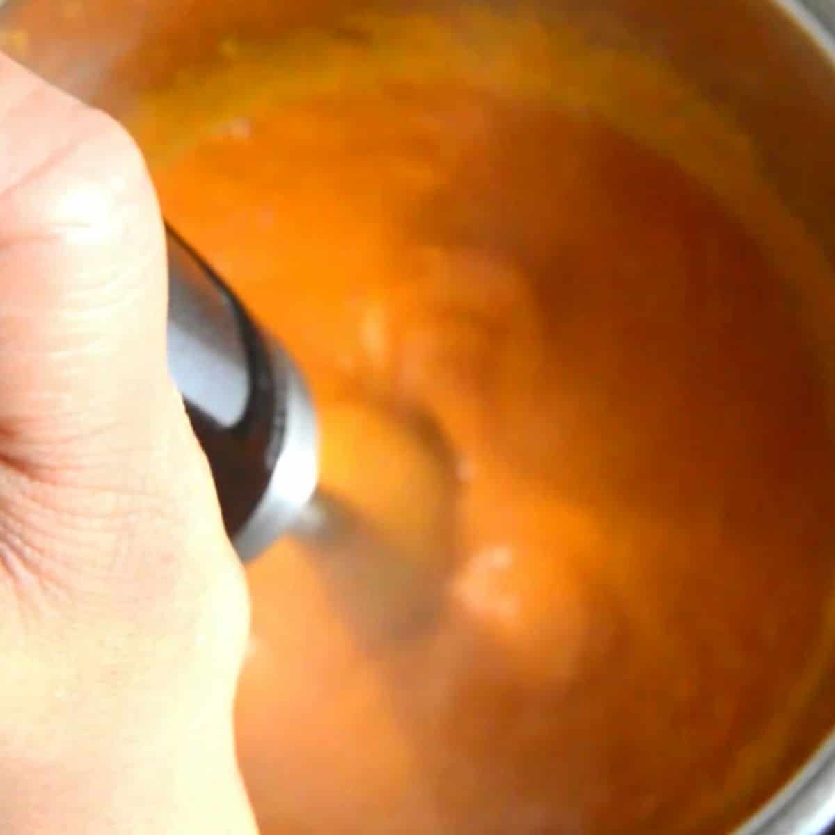 blending carrot lentil soup with an immersion blender.