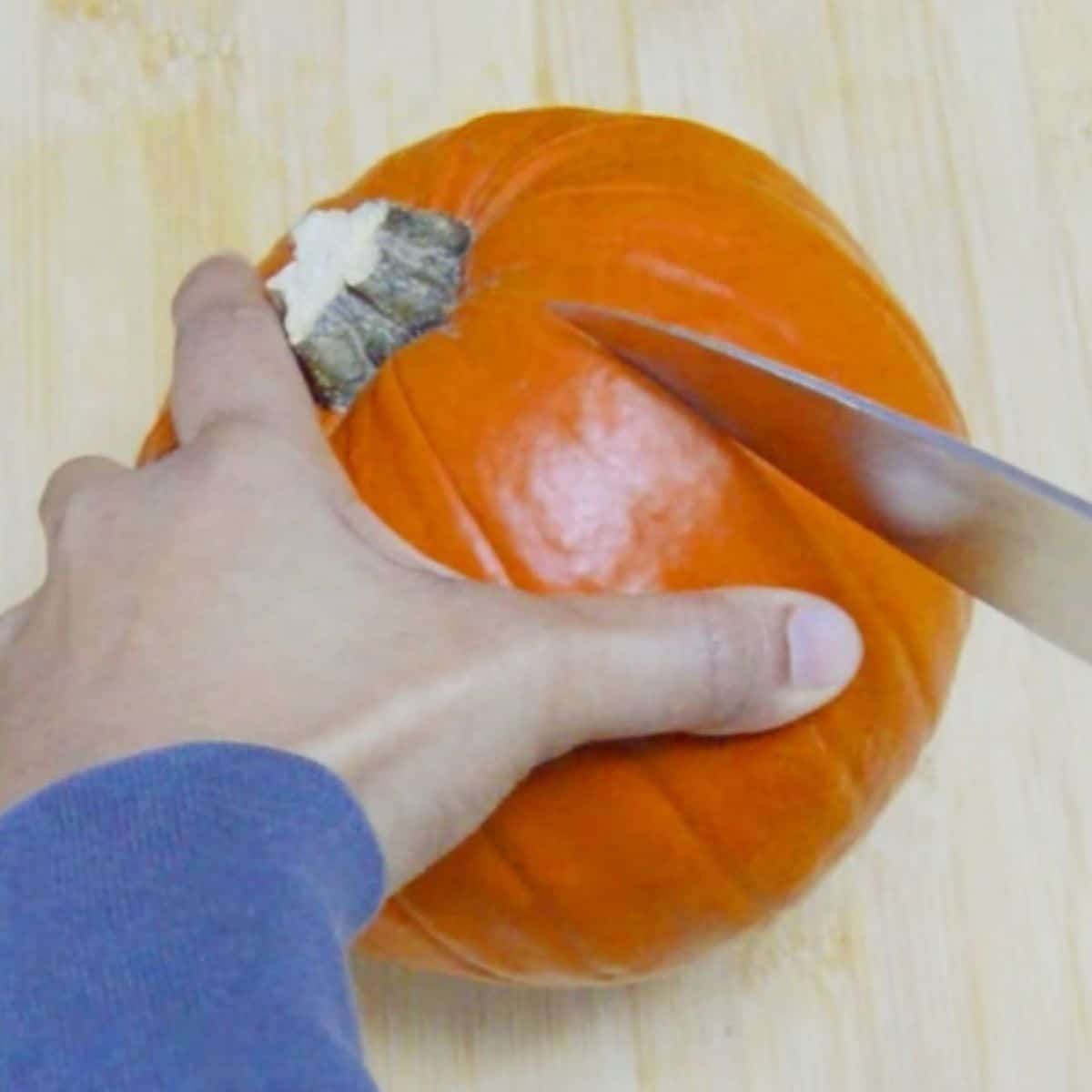 piercing pumpkin with a knife on a wooden boars.