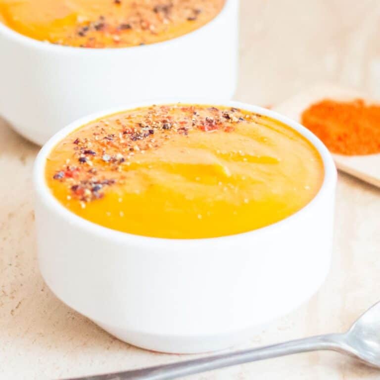 carrot-soup-in-white-bowl-placed-on-a-tile-with-spoon-next-to-it.
