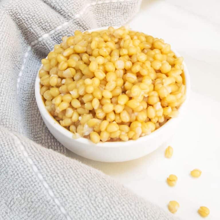 cooked wheat berries in a white bowl placed on a marble along with grey cloth.