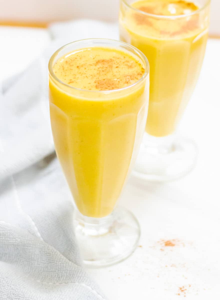 long shot of pumpkin banana smoothie in 2 tall glasses placed on a marble along with a cloth napkin.