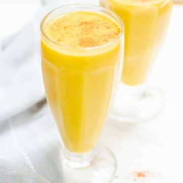 close up shot of pumpkin banana smoothie in 2 tall glasses placed on a marble along with a cloth napkin.
