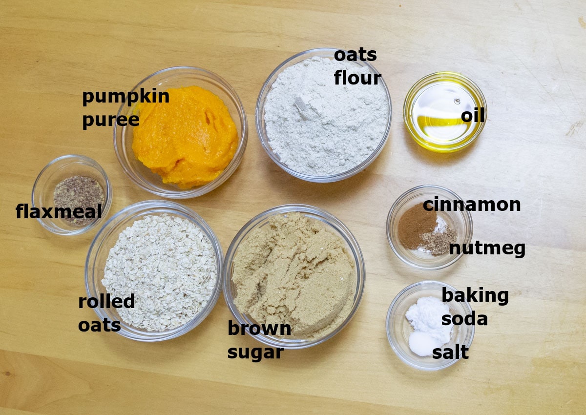 oats, flour, pumpkin puree, spices, oil, flaxmeal and brown sugar in bowls placed on a wooden table.