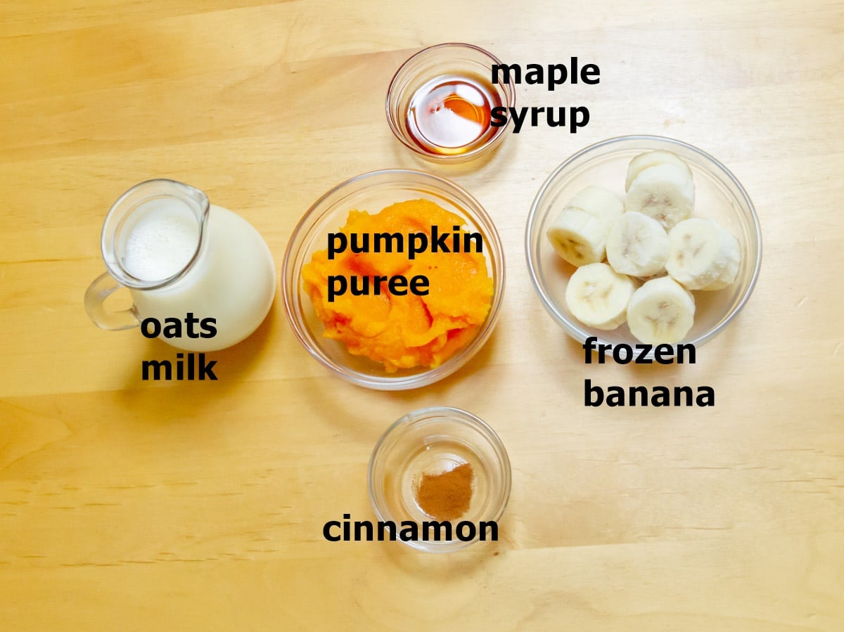 pumpkin puree, maple syrup, milk, banana and spice mix in individual bowls placed on a wooden table.