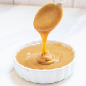 close up shot of pouring a spoon of caramel sauce into a white bowl filled with date caramel sauce.