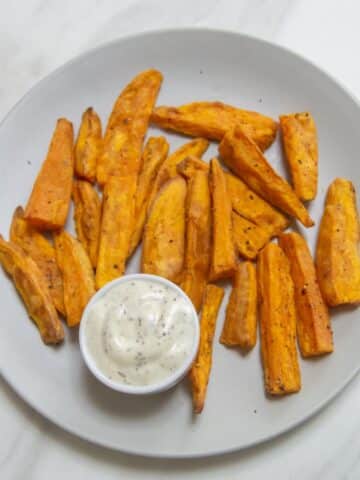 sweet potato wedges in a plate along with a white dip placed on a marble.