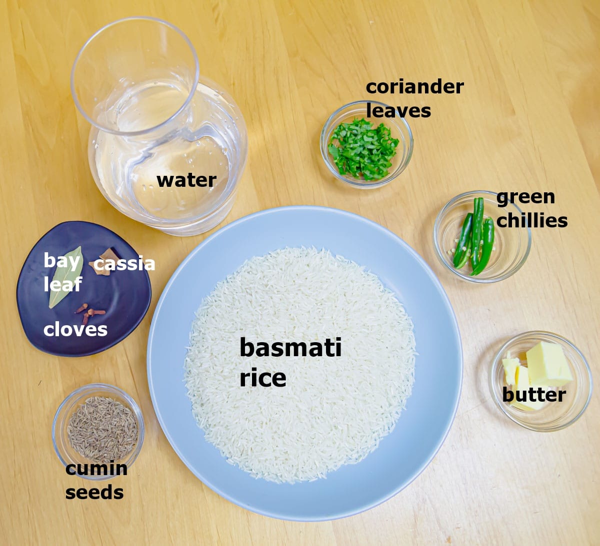 basmati rice, whole spices, water, butter, green chillies and coriander placed on a wooden table.