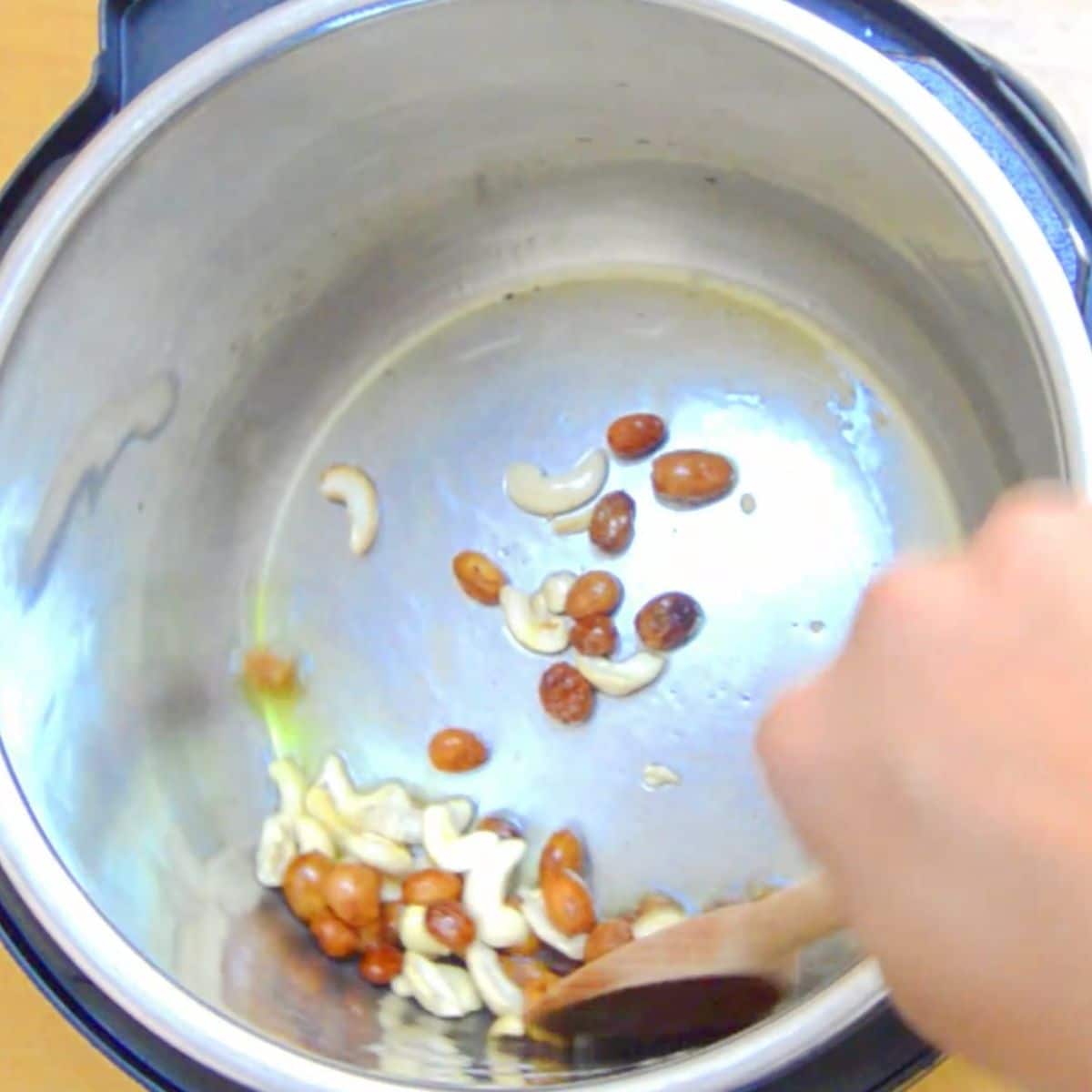 frying raisins and cashew nuts with a wooden spoon in the steel pot.