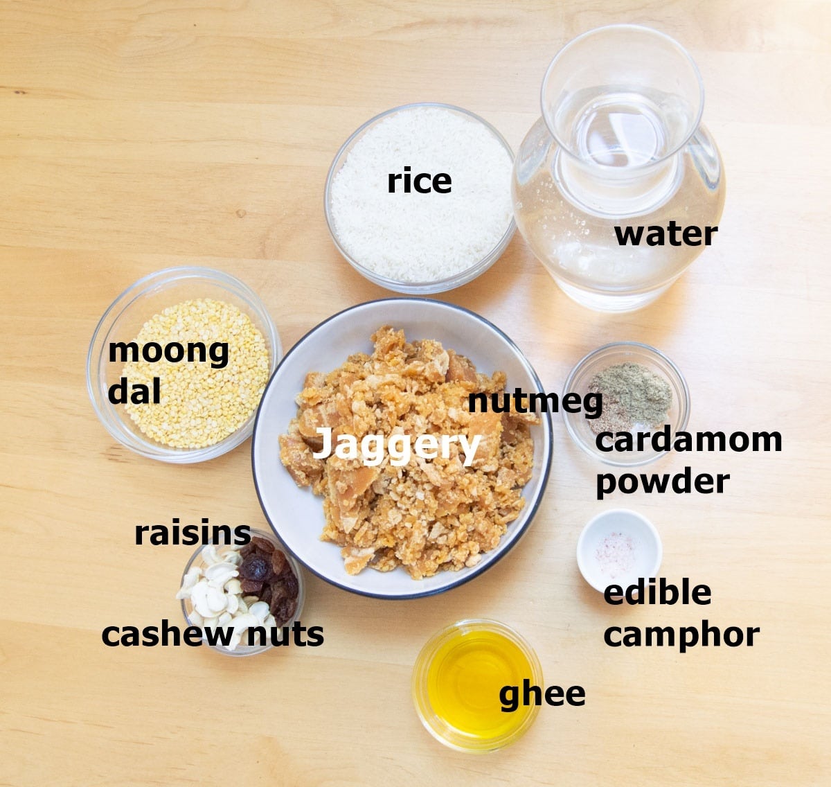 jaggery, rice, lentils, water, camphor, ghee, cardamom, cashews and raisins placed on a wooden table.