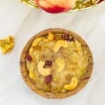 top shot of sweet pongal in a sal leaf bowl placed on a marble along with a fruit basket behind.