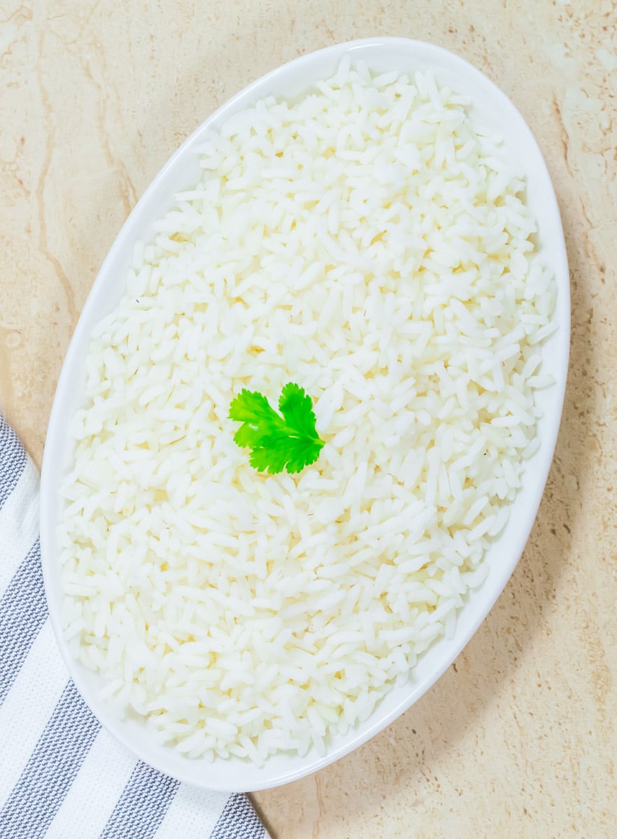 perfectly cooked parboiled rice in a oval bowl with a coriander leaf in the middle placed on a tile along with a cloth. 