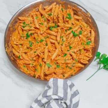 top shot of steel pan of pink sauce pasta placed on a marble along with a sprig of parsley.