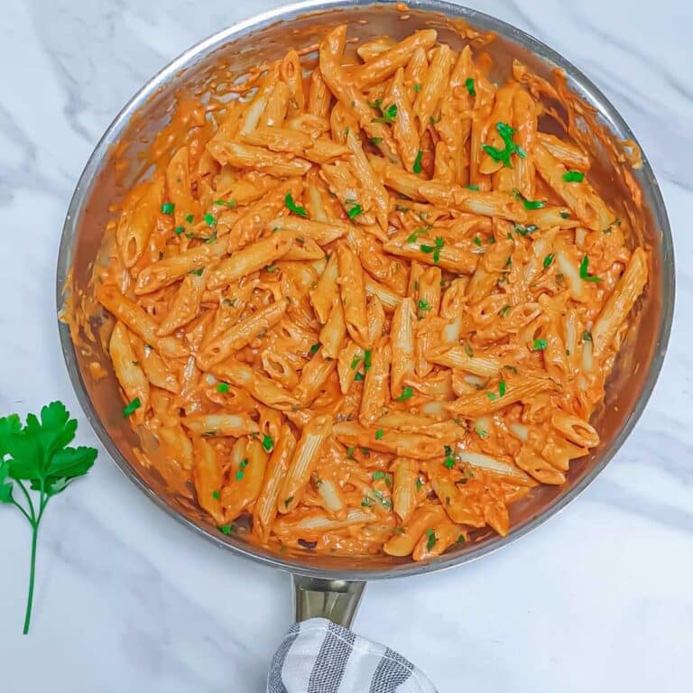 top shot of steel pan of pink sauce pasta placed on a marble along with a sprig of parsley.