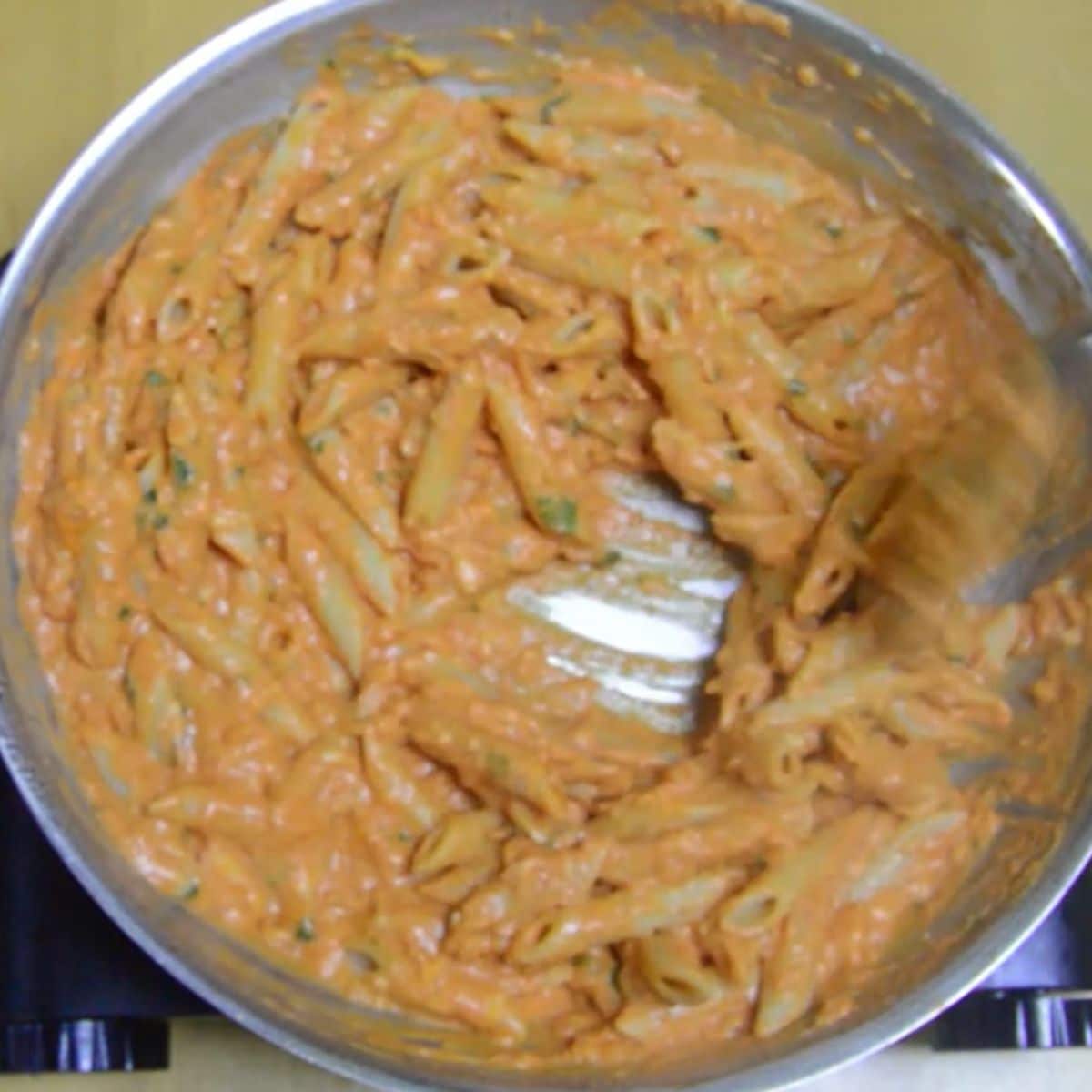 mixing pasta with sauce in a steel pan with a wooden spoon.