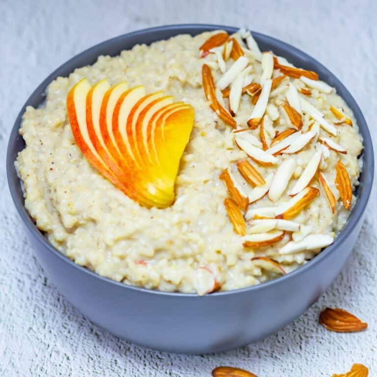 grey bowl of millet porridge with almonds and apple slices topped on it.