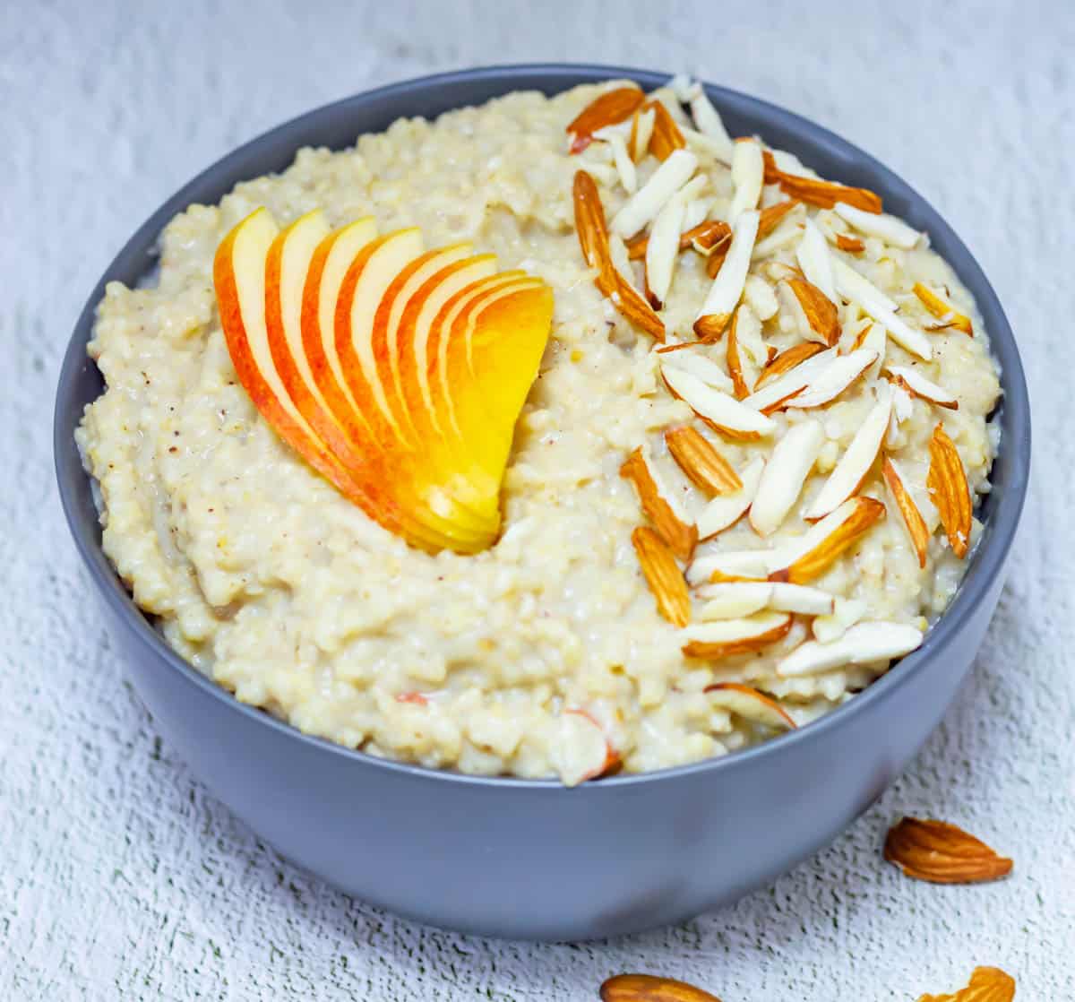 millet porridge in a grey bowl placed on a tile with almond slices next to the bowl.