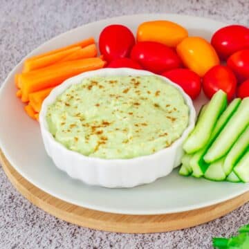 avocado dip with vegetable sticks and cherry tomatoes placed on a plate on a wooden boars.