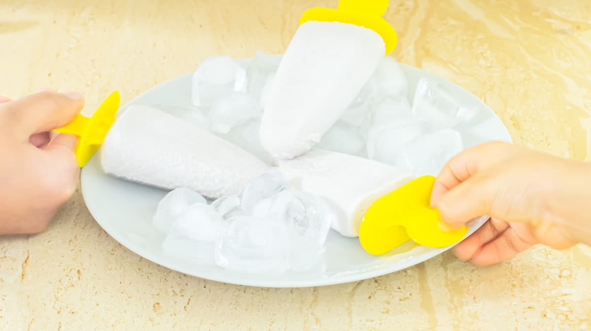 kids holding banana popsicles that are placed in a plate with ice cubes.