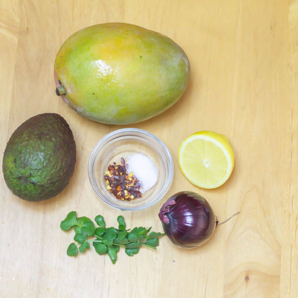 mango, avocado, coriander, red onion, lemon and seasoning placed on a wooden table.