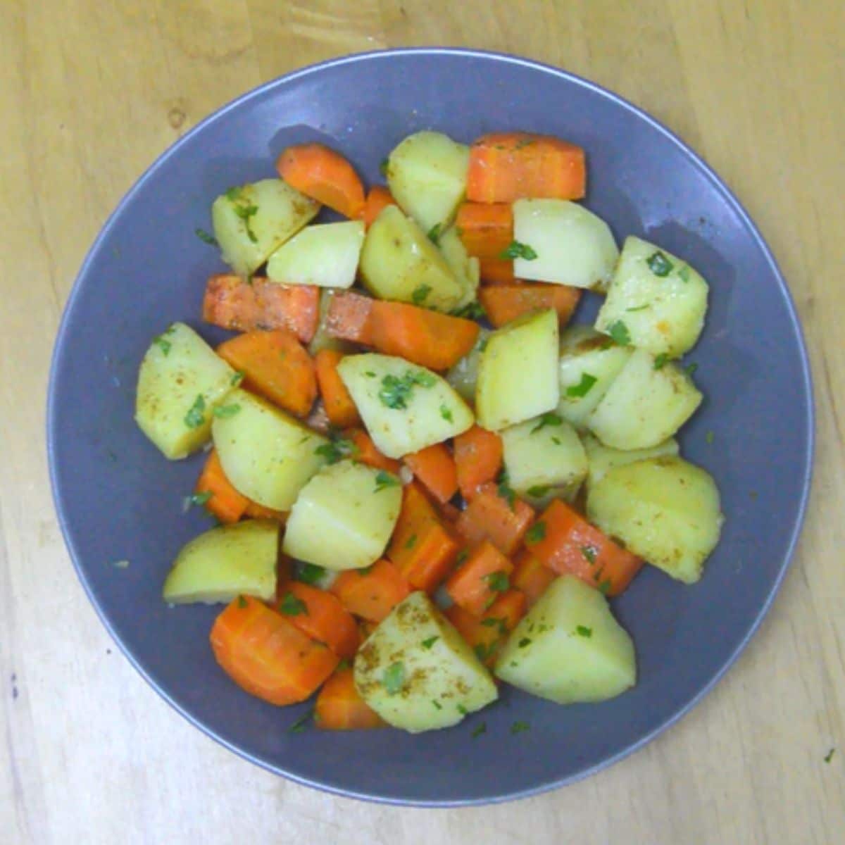 healthy steamed vegetables in a grey bowl placed on a wooden table.