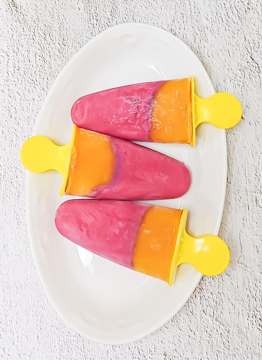 3 cherry mango popsicles placed on a white plate on a tile.