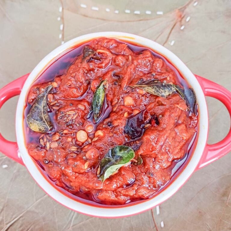 fresh tomato pickle in a red pot placed on a leaf plate.