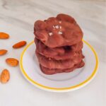 stack of chocolate almond clusters in a plate placed on a marble with a few almonds next to it.