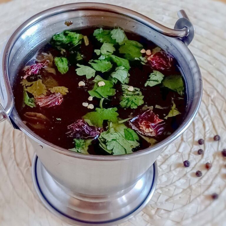 bucket of pepper rasam placed on a wooden placemat.