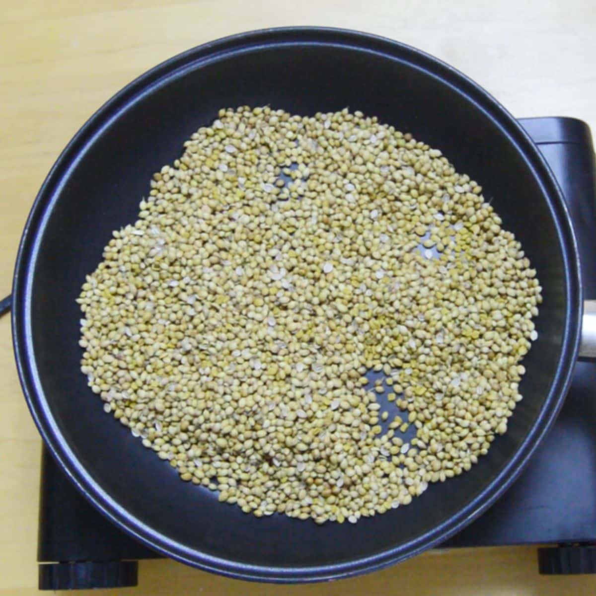 coriander seeds in a black pan placed on black burner.