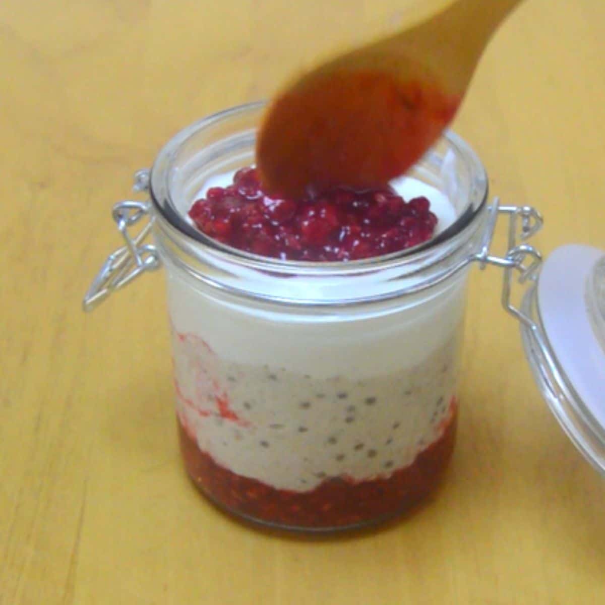 adding pureed raspberry with wooden spoon on top of yogurt layer.