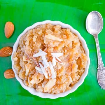 close up shot of almond halwa with topped almonds placed on a green leaf plate along with a spoon and few almonds.