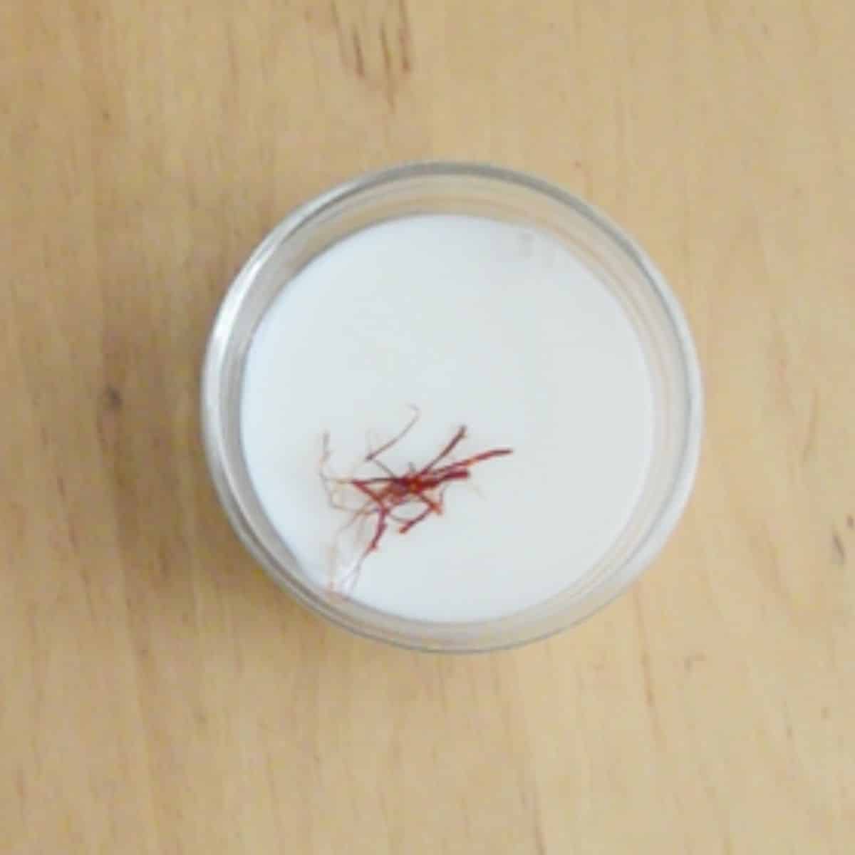 saffron strands in a cup of milk placed on wooden table.