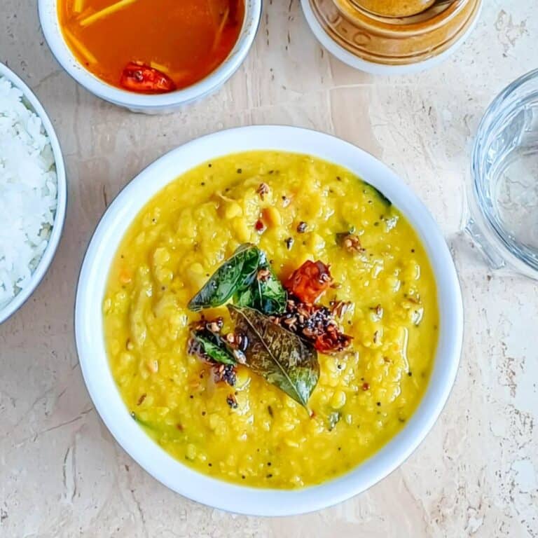 cucumber dal in a white bowl placed on a granite along with bowl of rice, glass of water and a bowl of rasam.