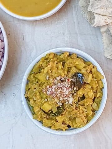 lauki ki sabji in a white bowl placed on a tile along with a bowl of red rice, curry and rotis.