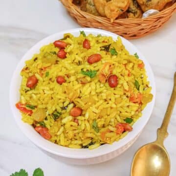 white bowl of uggani placed on marble along with a brass spoon and a basket of bajjis.