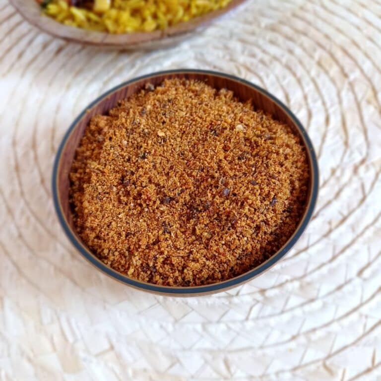 brown bowl of puliyogare mix placed on wooden palcemat along with a bowl of puliyogare rice.