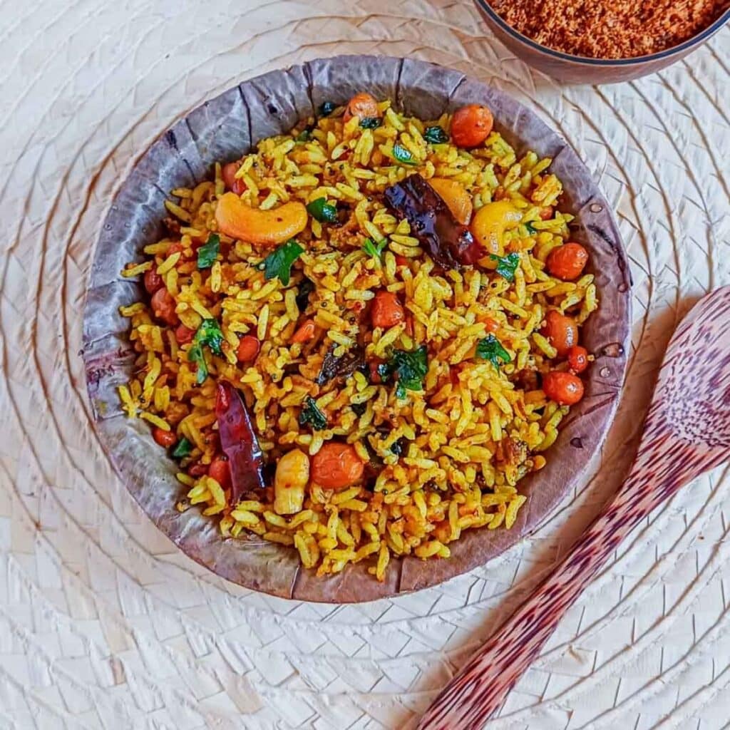 a bowl of puliyogare rice placed on wooden placemat along with a wooden spoon.