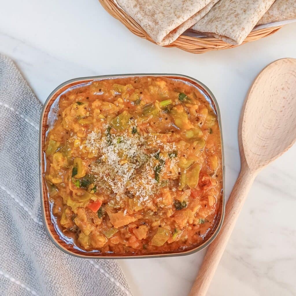 beerakaya kura in a square bowl placed on a white marble along with wooden spoon, napkin and a plate of chapatis.