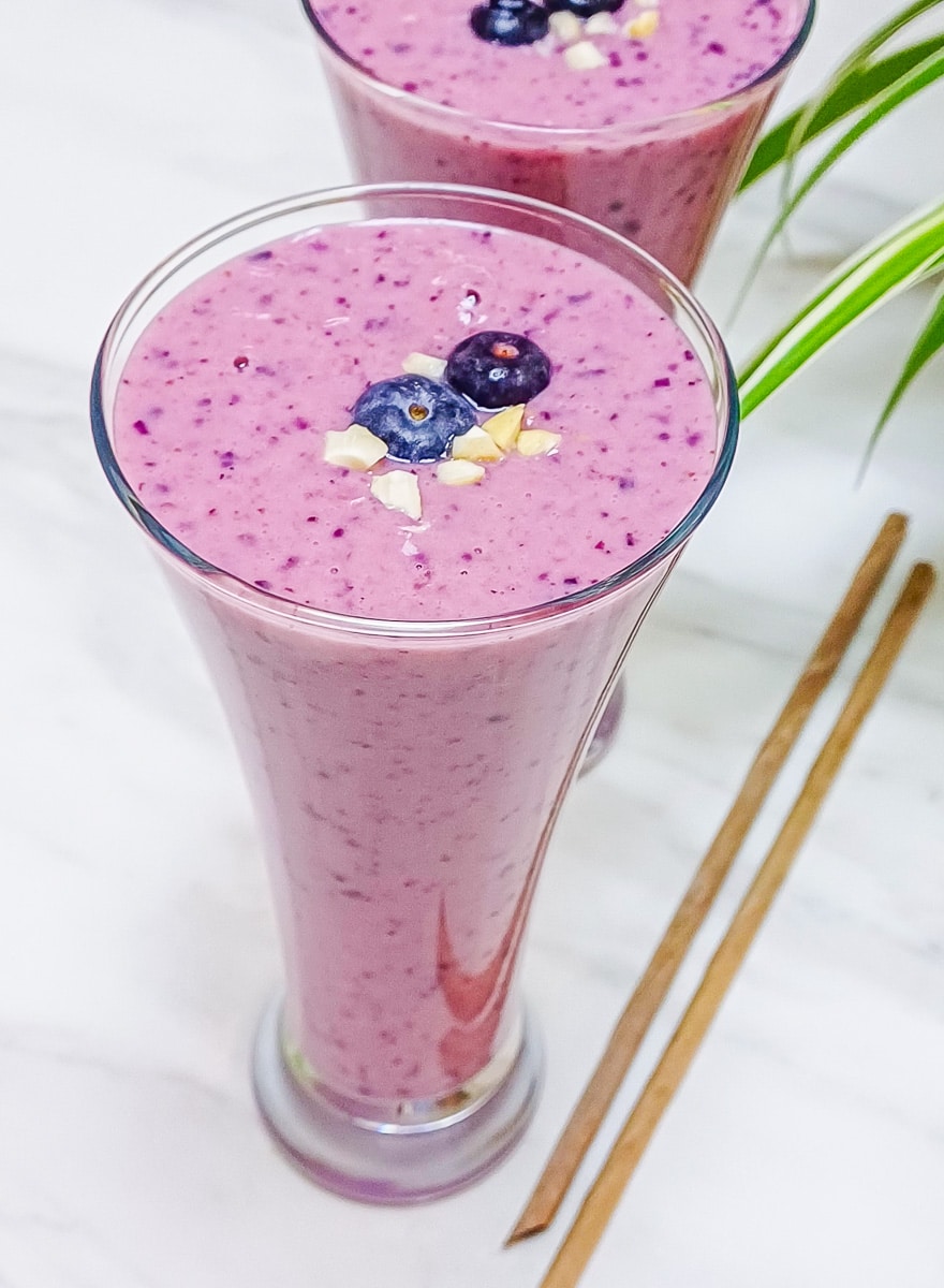 blueberry raspberry banana smoothie in a glass with fresh blueberries on top placed on marble with 2 straws.
