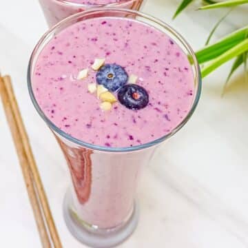tall glass of blueberry raspberry smoothie with fresh blueberry topping.