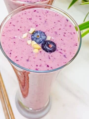 tall glass of blueberry raspberry smoothie with fresh blueberry topping.