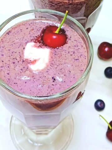 cherry berry smoothie in a glass with yogurt and cherry on the top.