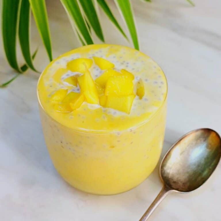 mango chia seed pudding in a glass placed on marble along with a spoon next to it.