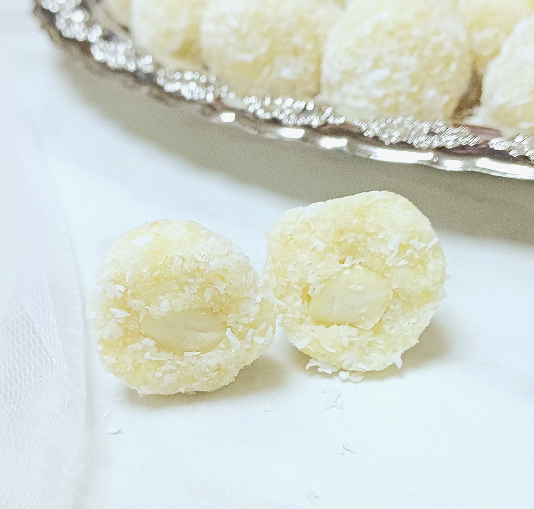 coconut almond ball cut into half placed on marble along with a plate of balls.