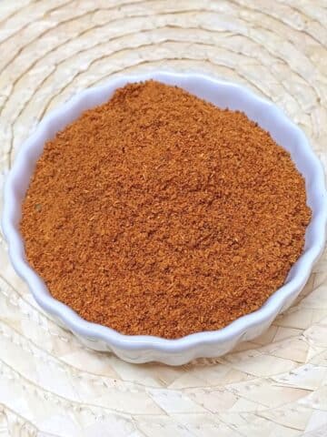 white bowl of vangibath masala powder placed on a wooden mat.