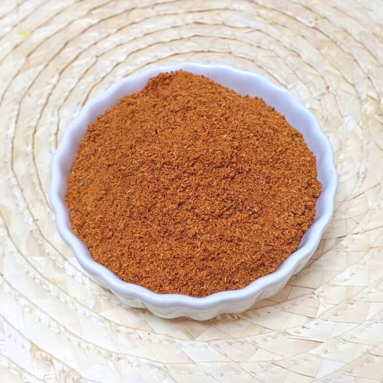 white bowl of vangibath masala powder placed on a wooden mat.
