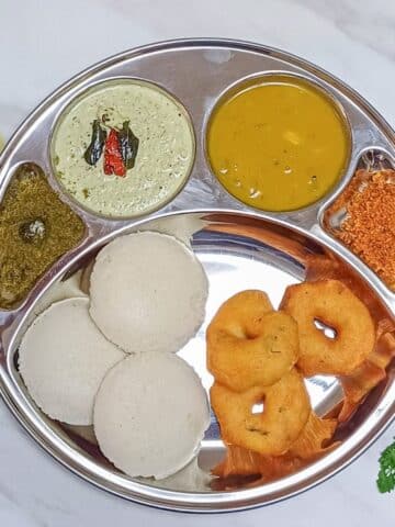 idli, vada, sambar and chutney in a steel compartment plate.