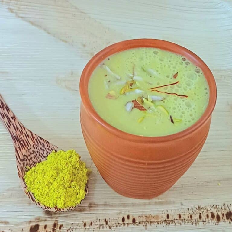 clay glass filled with masala milk placed on wooden board along with a spoonful of milk masala.